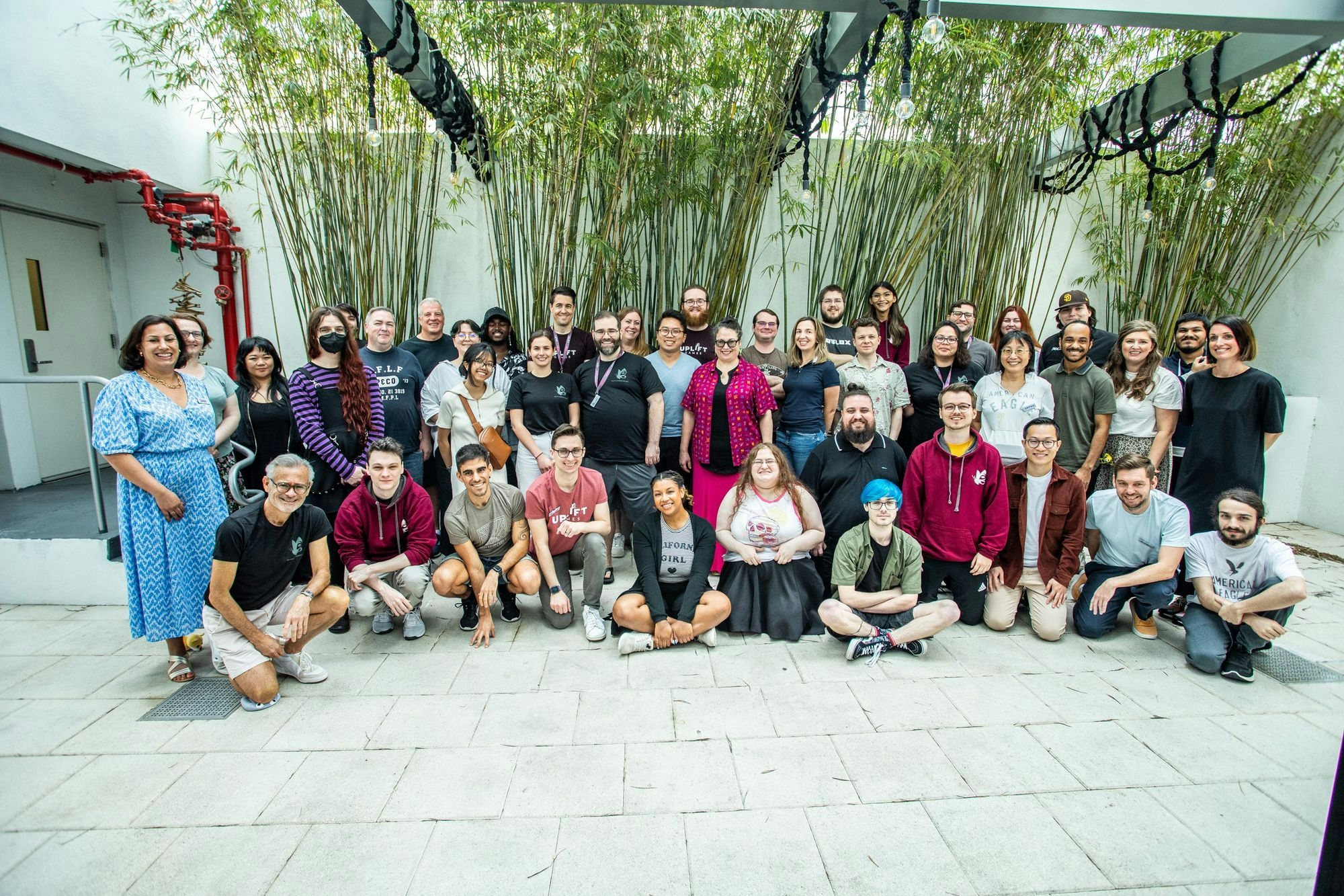 A group pfoto of Team Uplift at the Uplift Conference 2023. 43 people standing and kneeling for a group photo in a courtyard surrounded by green bamboo plants, everyone is smiling.. 